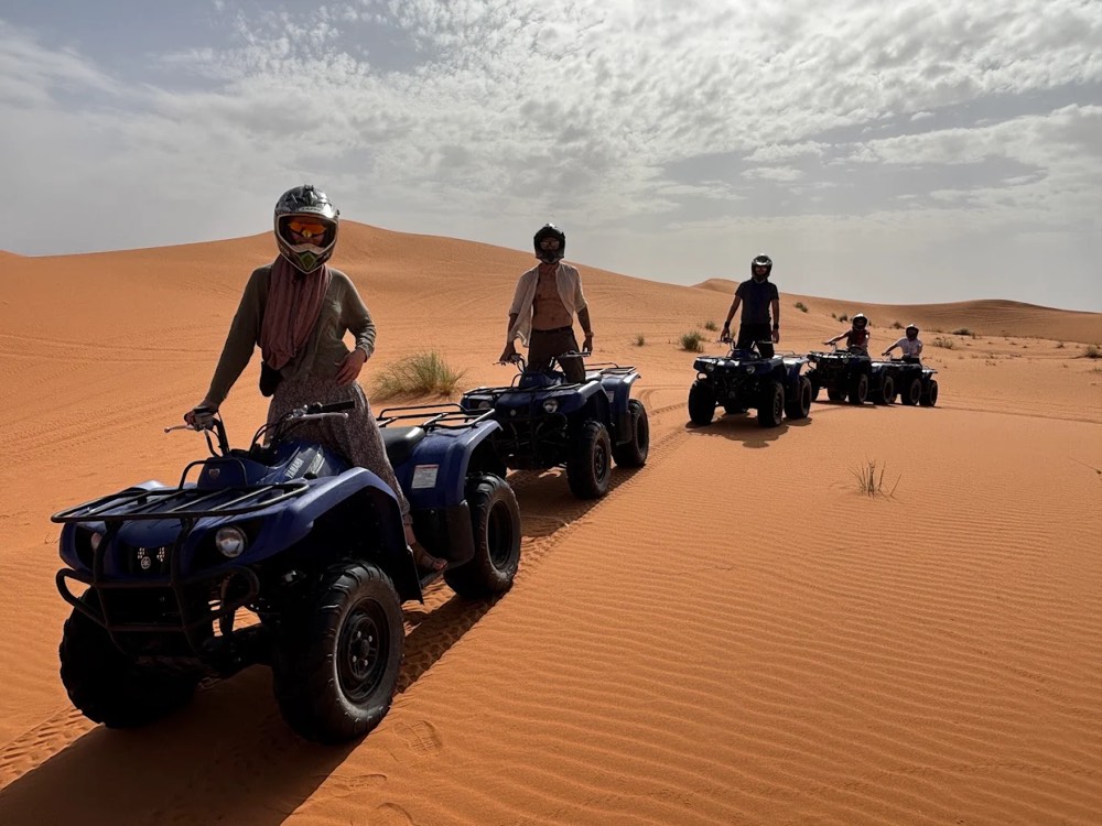 Rijders op quads op een rij in de duinen van Merzouga onder een bewolkte lucht