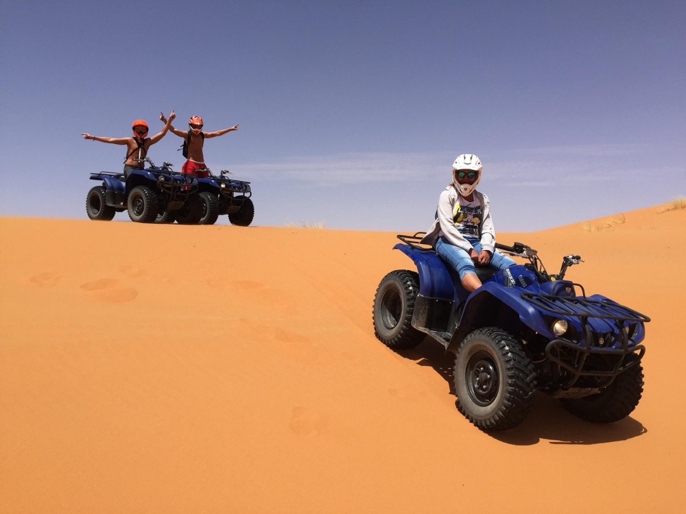 Quad riders celebrating on top of an orange dune in Erg Chebbi