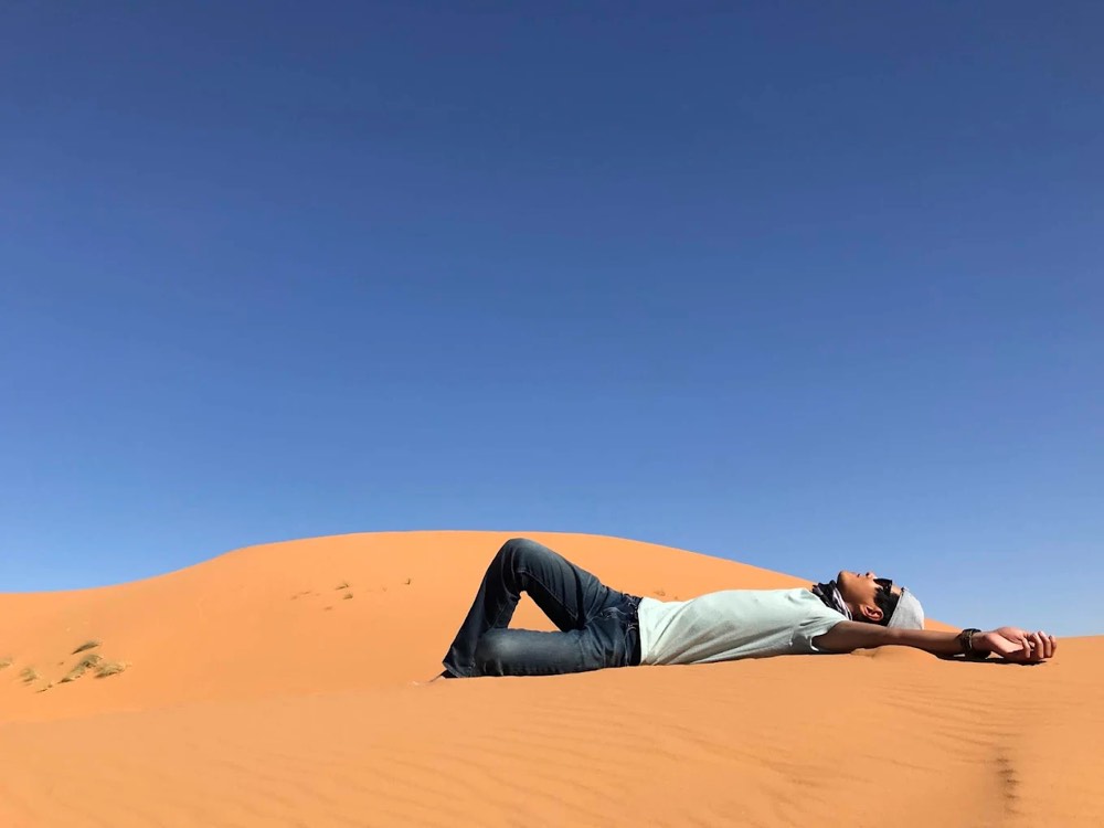 Traveller relaxing on the warm sand of a dune in Merzouga under a blue sky