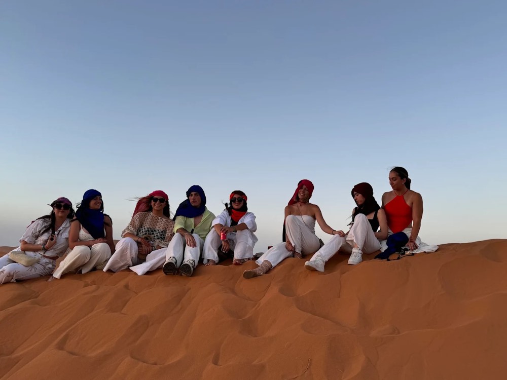 Group of travellers sitting together on a dune in Merzouga at golden hour