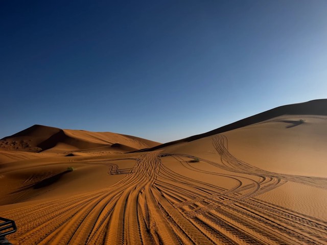 Huellas curvas de quad en la ladera de una duna del Erg Chebbi con la luz de última hora de la tarde