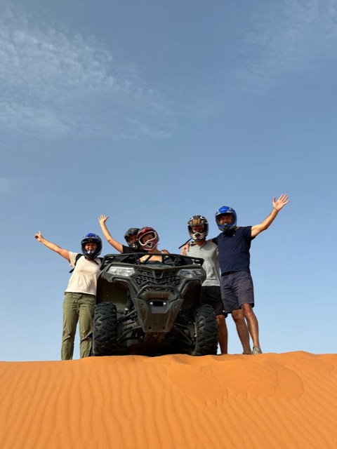 Quatre amis célébrant à côté de leur quad au sommet d’une dune de l’Erg Chebbi