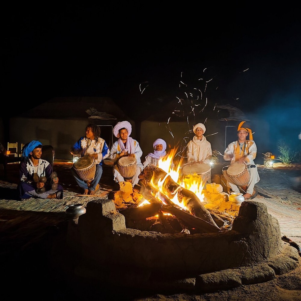 Muzikanten trommelen ’s avonds rond het kampvuur in een woestijnkamp in Merzouga