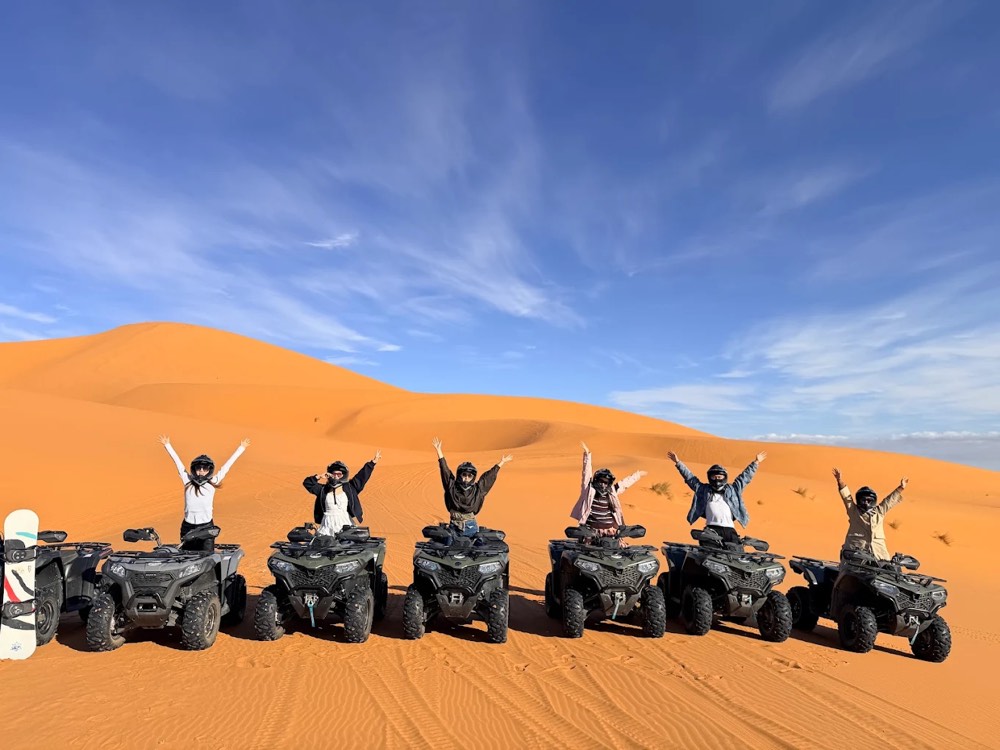 Sei piloti con le braccia alzate sui loro quad in fila su una duna a Merzouga