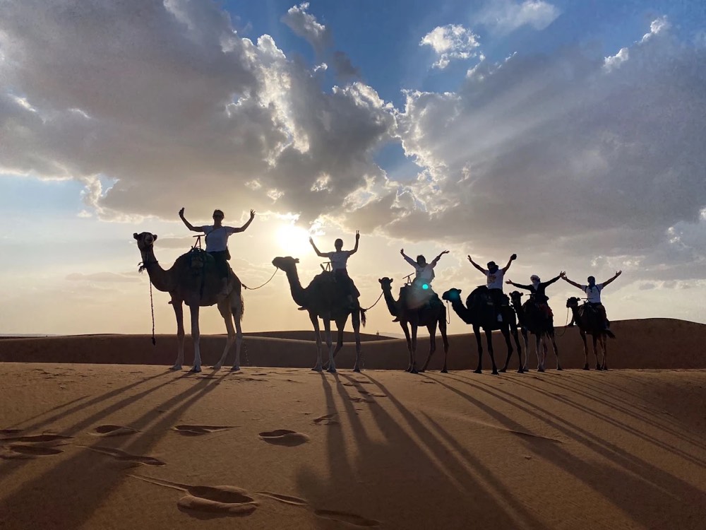 Kamelenkaravaan met ruiters trekt onder een dramatische lucht door de duinen van Merzouga