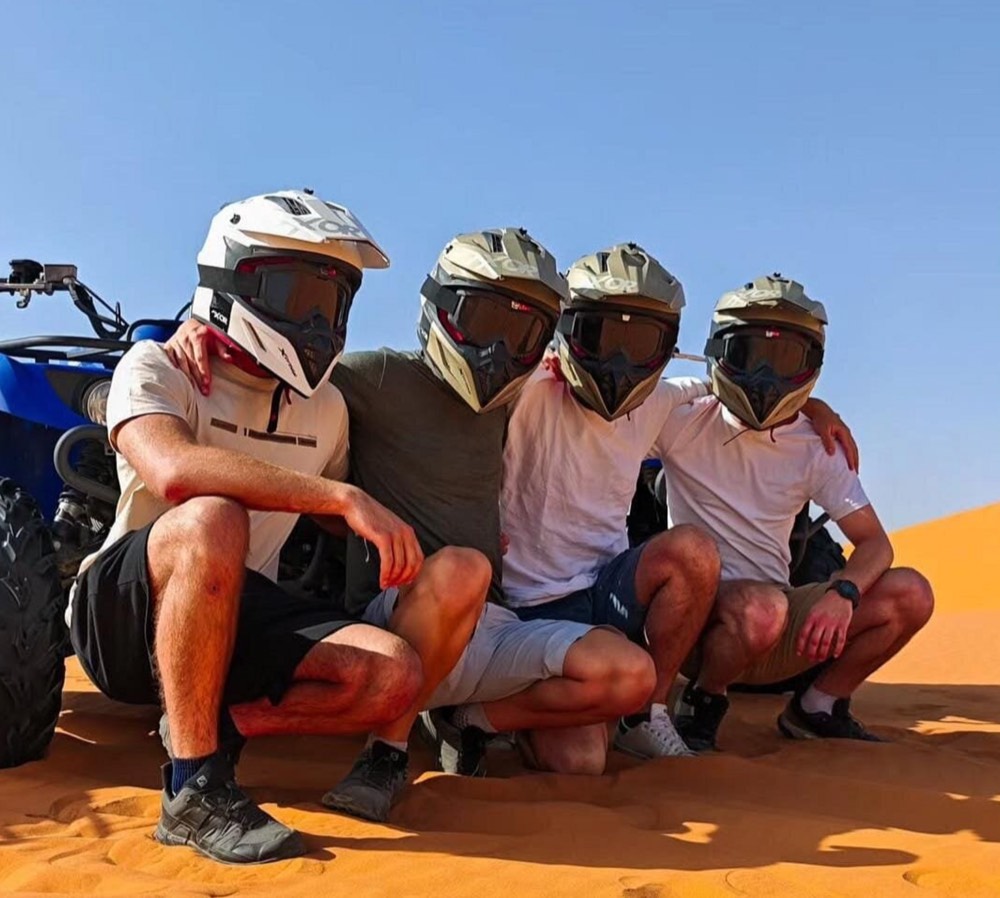 Four friends in quad helmets smiling together in the Merzouga desert