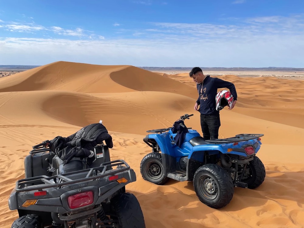 Due quad parcheggiati su una duna e un pilota con il casco in mano nell’Erg Chebbi