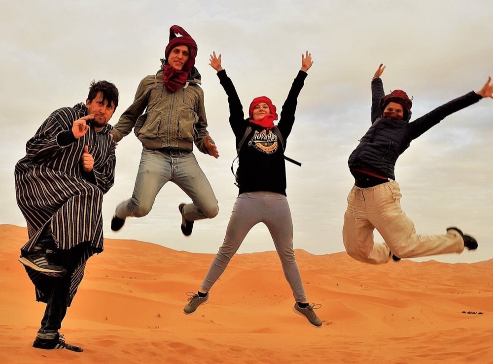 Voyageurs heureux sautant en l’air sur une dune à Merzouga