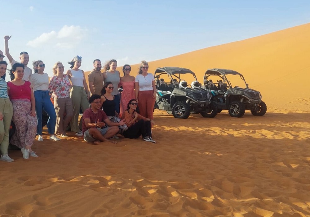 Gruppe von Reisenden posiert neben ihren Dünenbuggys in der Wüste von Merzouga