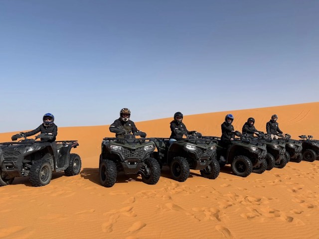 A group of riders lined up on quad bikes at the foot of a dune in Merzouga
