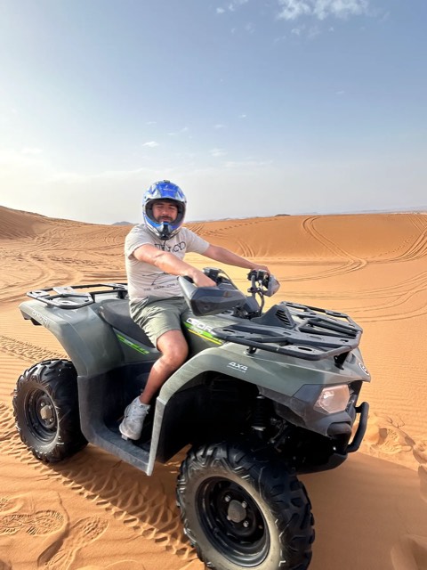 Pilota sorridente con il casco su un quad tra le dune di Merzouga