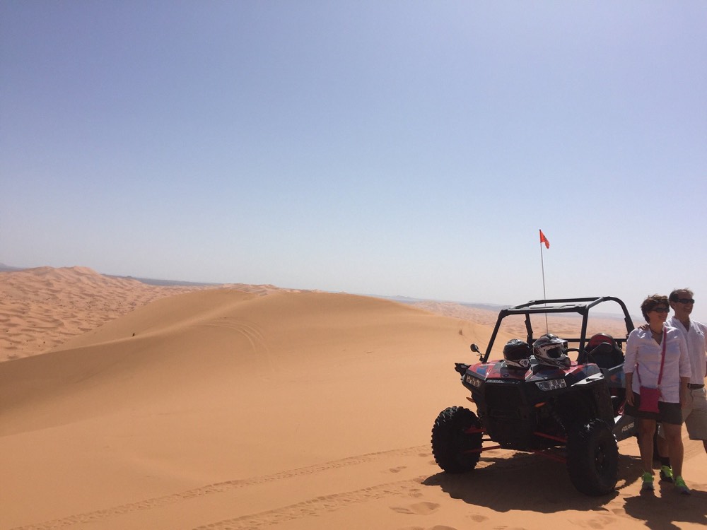 Duas pessoas junto a um buggy numa duna alta, na luz suave da manhã do Erg Chebbi