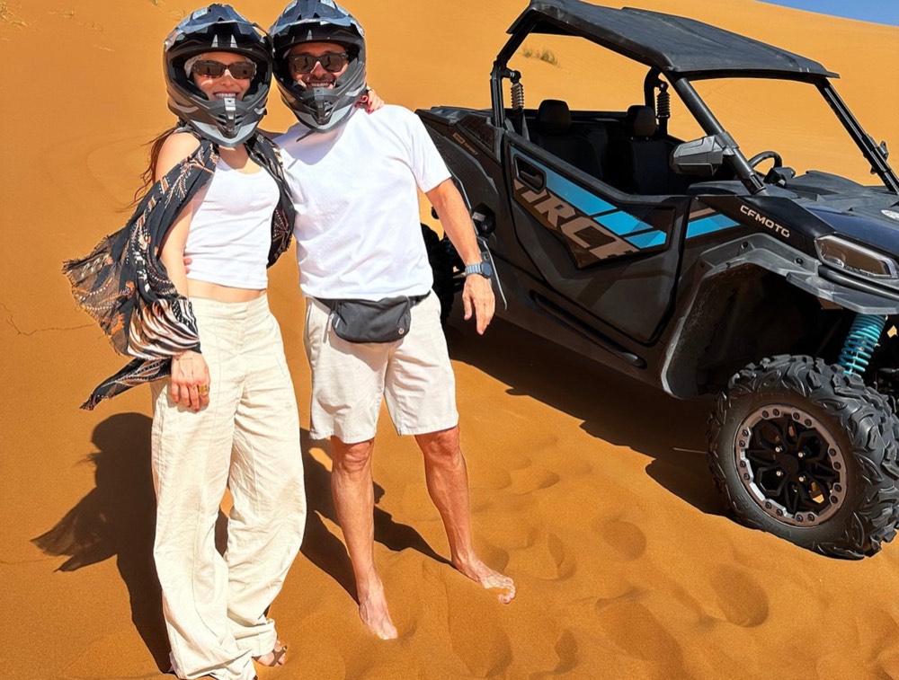 Couple in helmets standing next to their dune buggy on the sand in Merzouga