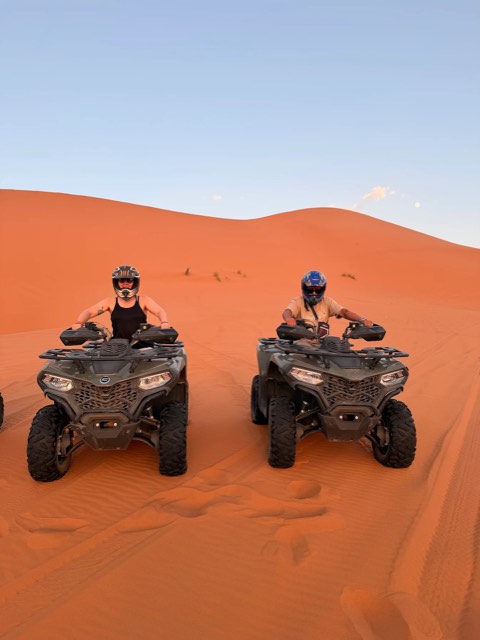 Zwei Quadfahrer nebeneinander zwischen orangefarbenen Dünen in Merzouga
