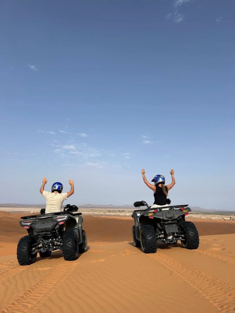 Zwei Quadfahrer reißen auf einem Dünenkamm in der Sahara die Arme hoch